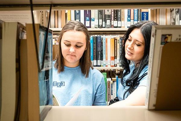 Two students looking through books in the library 